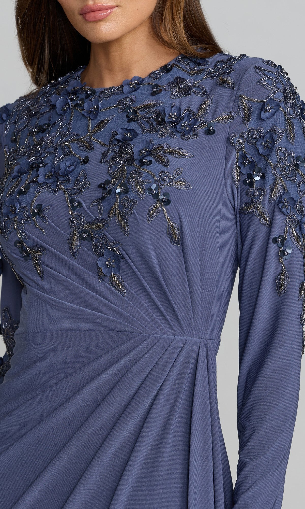 A woman wearing the Mac Duggal 13246 long formal dress, featuring long sleeves, a deep blue hue, and detailed floral applique with beaded embellishments adorning the shoulder and upper bodice.